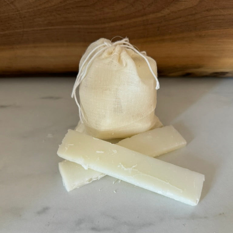 Three blocks of tallow soap on a marble surface with a wooden board in the background.
