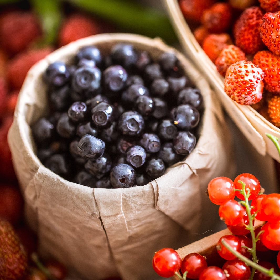 Assorted berries including blueberries and red currants in paper bags.